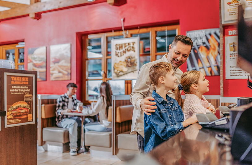 Ein Vater mit seinen Kindern bei der Bestellung am Burger King Tresen in der Oldtimer Raststation Oed.